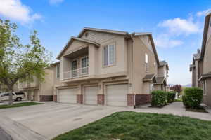 View of front of home featuring brick siding, a garage, a balcony, and stucco siding