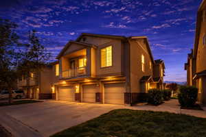 View of front of house featuring brick siding, a balcony, a garage, stucco siding, and driveway