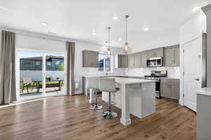 Kitchen featuring gray cabinets, a breakfast bar, stainless steel appliances, tasteful backsplash, and a center island