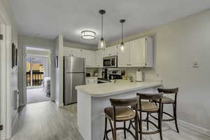 Kitchen with a kitchen bar, stainless steel appliances, light countertops, white cabinetry, and a peninsula