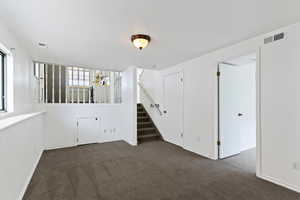 Empty room featuring stairway and dark colored carpet
