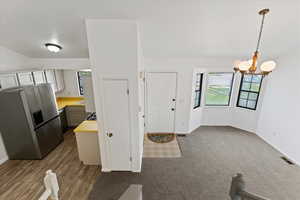 Kitchen featuring stainless steel refrigerator with ice dispenser, light countertops, white cabinetry, and suspended lighting