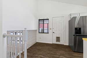 Kitchen with stainless steel refrigerator with ice dispenser, dark wood-style flooring, white cabinetry, lofted ceiling, and light countertops