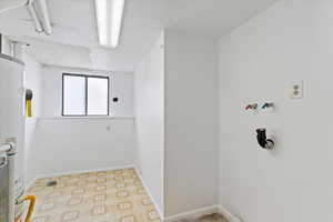 Laundry area with light floors, gas water heater, a textured ceiling, and washer hookup