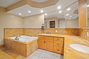 Primary bathroom featuring double vanity, recessed lighting, stone tile floors that are radiant heated, and a jetted tub