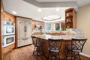 Kitchen with a peninsula, a kitchen breakfast bar, light wood-style flooring, white double oven, and paneled fridge