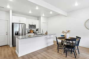 Kitchen featuring stainless steel appliances, light stone countertops, light wood-style floors, white cabinetry, and an island with sink