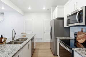 Kitchen featuring stainless steel appliances, white cabinetry, light stone countertops, and recessed lighting