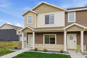 View of front of home with stone siding, a front lawn, a shingled roof, and board and batten siding