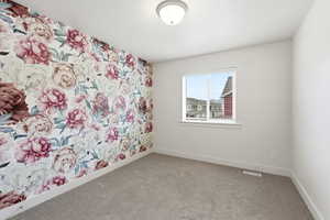 Empty room with wallpapered walls, an accent wall, and light colored carpet