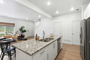 Kitchen with white cabinetry, a center island with sink, stainless steel appliances, light stone counters, and light wood finished floors