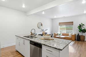 Kitchen featuring white cabinets, light stone counters, dishwasher, a kitchen island with sink, and light wood-type flooring
