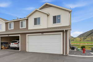 View of front facade with a shingled roof, a garage, a mountain view, asphalt driveway, and board and batten siding