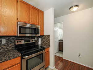 Kitchen with stainless steel appliances, wood finish cabinetry, light wood-style flooring, and dark stone countertops