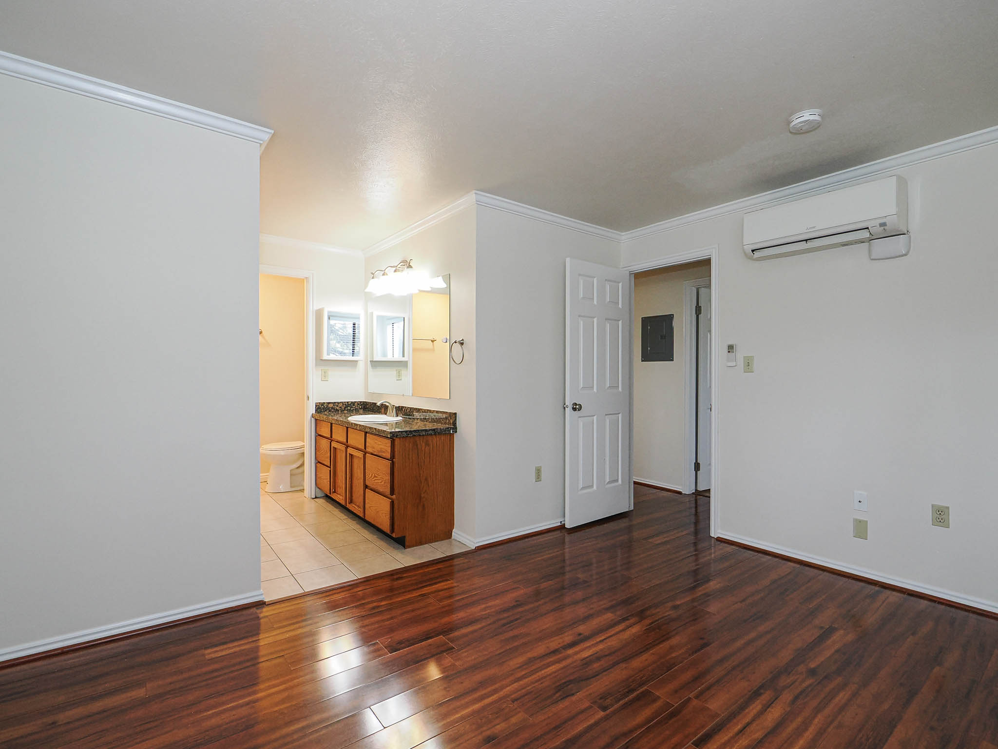 Unfurnished bedroom featuring light wood-type flooring, ornamental molding, electric panel, and ensuite bathroom