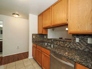 Kitchen with stainless steel dishwasher, light tile patterned flooring, decorative backsplash, dark stone counters, and wood finish cabinetry