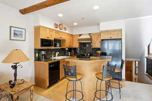 Kitchen featuring black appliances, tasteful backsplash, tile counters, light wood-style floors, and a breakfast bar area