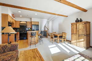 Kitchen with tasteful backsplash, black appliances, beamed ceiling, a kitchen bar, and light carpet