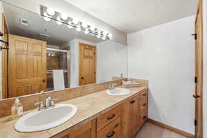 Full bath featuring a stall shower, double vanity, and a textured ceiling