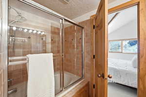 Bathroom with connected bathroom, bath / shower combo with glass door, and a textured ceiling