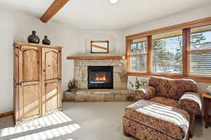 Living room featuring a stone fireplace, carpet floors, and beam ceiling