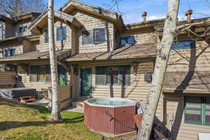 Rear view of house with a hot tub, a patio, and a lawn