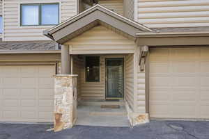 Property entrance with a shingled roof, an attached garage, and faux log siding
