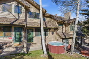 Back of house featuring a hot tub, a chimney, and roof with shingles