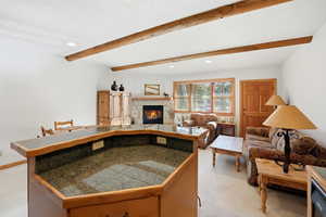 Kitchen featuring open floor plan, a kitchen island, a stone fireplace, beam ceiling, and recessed lighting