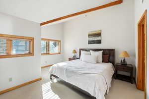 Bedroom with light colored carpet and lofted ceiling with beams