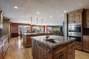 Kitchen with double oven, dark stone countertops, tasteful backsplash, light wood finished floors, and plenty of natural light