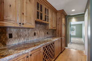Bar featuring glass insert cabinets, light wood-style floors, recessed lighting, wood finish cabinetry, and tasteful backsplash