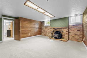 Unfurnished living room featuring wooden walls, light colored carpet, a wood stove, and a textured ceiling