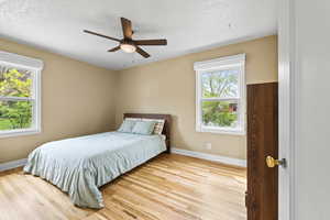 Bedroom with light wood-style floors, ceiling fan, and a textured ceiling