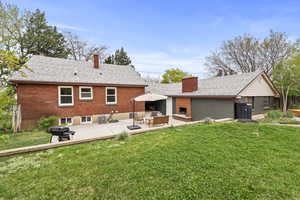 Back of house featuring brick siding, a yard, a shingled roof, and a patio area
