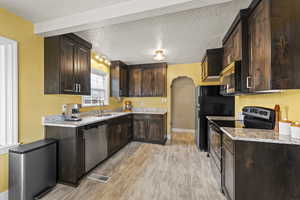 Kitchen with dark wood finish cabinets, stainless steel appliances, a textured ceiling, arched walkways, and light stone countertops