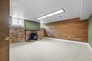 Unfurnished living room featuring carpet flooring, a wood stove, wood walls, and a textured ceiling