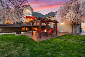 Rear view of property featuring a pergola, a yard, an outdoor fire pit, and stucco siding