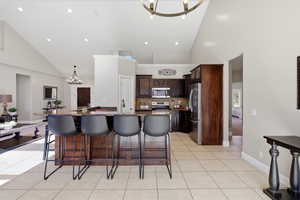 Kitchen featuring hanging lights, dark wood finish cabinetry, a kitchen breakfast bar, dark stone counters, and stainless steel appliances