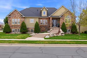 View of front of house featuring a front yard, stucco siding, stone siding, and a shingled roof