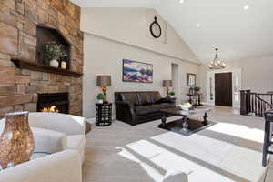 Living area with a stone fireplace, light colored carpet, vaulted ceiling, and a chandelier