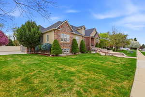 View of side of home with stone siding, a yard, stucco siding, and roof with shingles