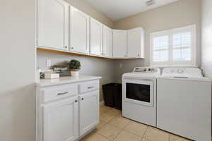 Laundry room with washer and dryer, light tile patterned floors, and cabinet space
