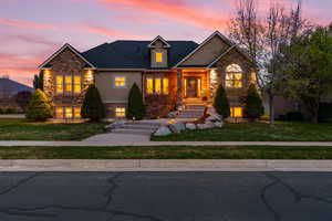View of front of house featuring stone siding, a yard, and roof with shingles