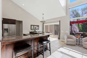 Kitchen with dark wood finish cabinets, stainless steel refrigerator with ice dispenser, a kitchen breakfast bar, dark stone counters, and vaulted ceiling