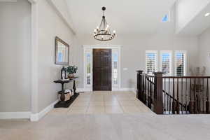 Entryway featuring a chandelier, light tile patterned floors, light carpet, and lofted ceiling