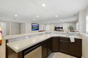 Kitchen with dark wood finish cabinetry, open floor plan, light countertops, dishwasher, and recessed lighting