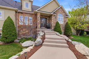 View of front of house with stone siding, roof with shingles, a front yard, and stucco siding