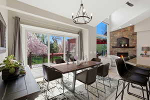 Dining area featuring a stone fireplace, hanging lights, light tile patterned flooring, and lofted ceiling