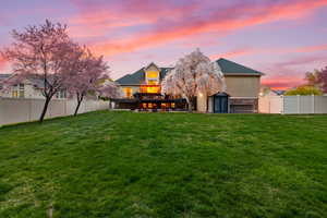 Back of house at dusk featuring a storage unit, a fenced backyard, and a wooden deck